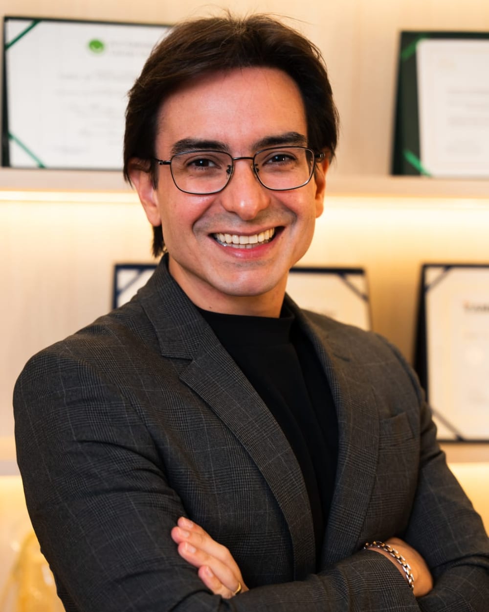 Dr. Luiz Henrique Schiavon, radiologista intervencionista, de braços cruzados diante dos diplomas do consultório